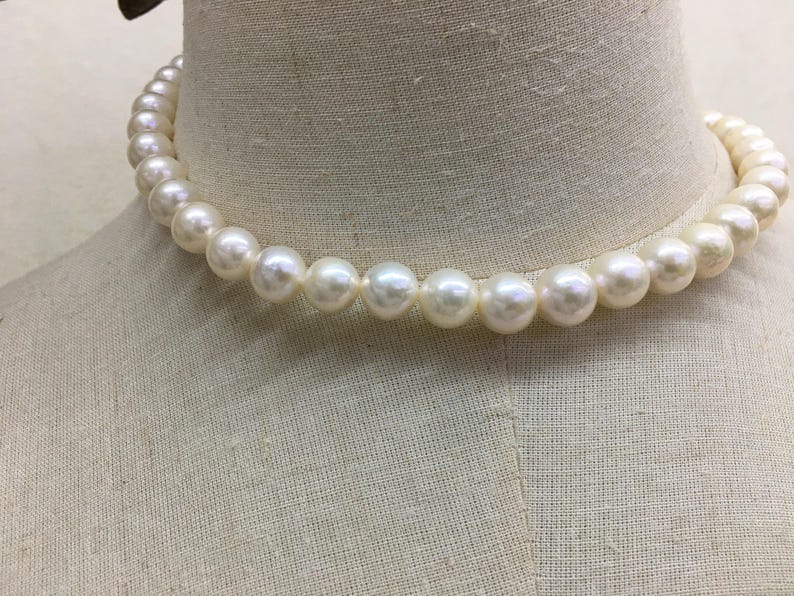 May include: A classic pearl necklace composed of round, off-white pearls. The necklace is draped around a mannequin's neck, showcasing its elegant design. The pearls are evenly sized and have a subtle luster, suggesting a timeless jewelry piece.