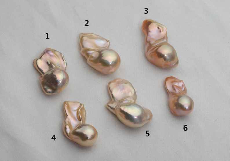 K&ouml;nnte beinhalten: Sechs Barockperlen in verschiedenen Formen und Gr&ouml;&szlig;en, mit irisierenden rosa und goldenen Farbt&ouml;nen. Die Perlen sind von 1 bis 6 nummeriert.