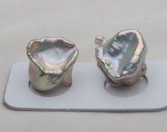 May include: Two iridescent white baroque pearls with a slightly green hue, displayed on a white card with circular cutouts.
