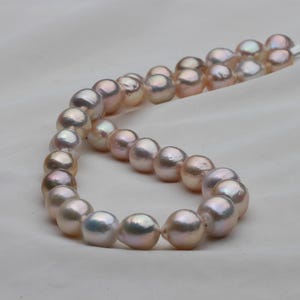 Puede incluir: Una hebra de perlas iridiscentes en tonos rosa y blanco. Las perlas están enhebradas en un hilo fino y están listas para convertirse en un collar o una pulsera.