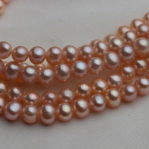 May include: A strand of pink freshwater pearls, with a soft, iridescent sheen. The pearls are round and smooth, and they are strung on a delicate thread.