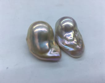 May include: Two iridescent baroque pearls with an off-white color. The pearls are irregular in shape and have a smooth, glossy surface.