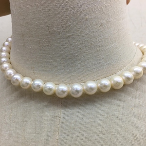 May include: A strand of creamy white pearls, evenly sized and strung together to form a necklace. The pearls are round and have a subtle luster, displayed on a mannequin bust.