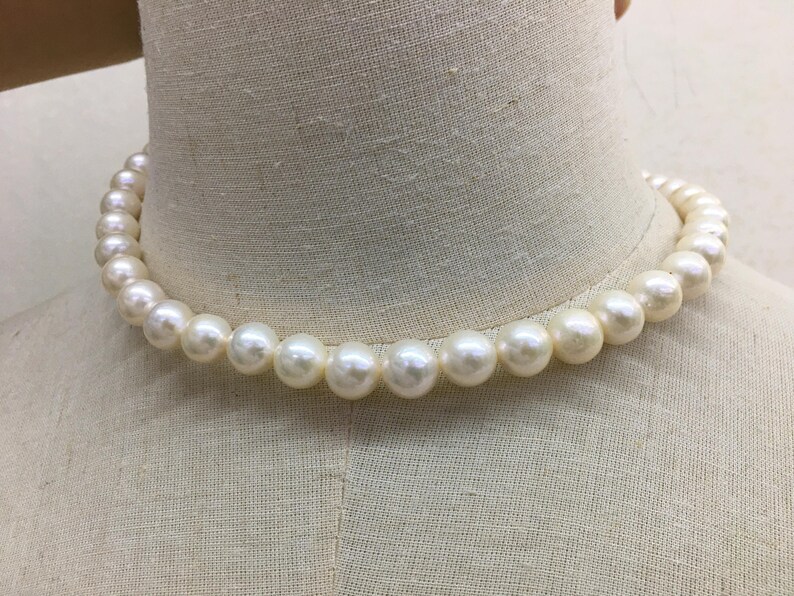 May include: A strand of creamy white pearls, evenly sized and strung together to form a necklace. The pearls are round and have a subtle luster, displayed on a mannequin bust.