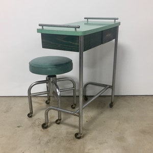 May include: A vintage green metal medical cart with a drawer and two chrome handles. The cart has a matching green vinyl stool with a chrome base and wheels.