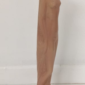 May include: A pink ceramic figurine of a woman standing with her arms at her sides. The figurine has a long, flowing gown and a detailed base.