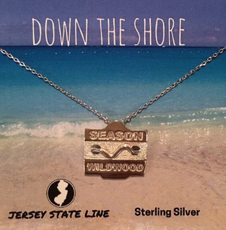 May include: Sterling silver necklace with a pendant that says "Season Wildwood" on a silver background. The necklace is on a white card with the text "Down the Shore" and "Jersey State Line" in black.