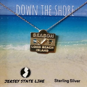 May include: Sterling silver necklace with a pendant that says "Season Long Beach Island". The pendant is shaped like a beach tag and has a wave design. The necklace is on a white background with the words "Down the Shore" and "Jersey State Line" printed on it.