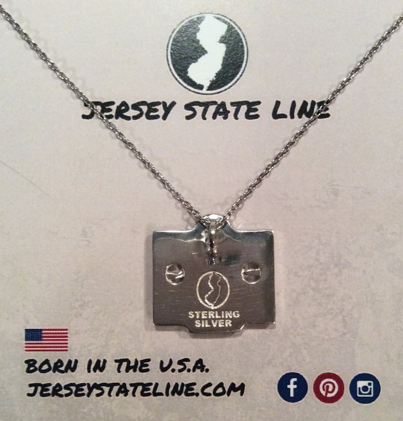 May include: Silver necklace with a pendant shaped like the state of New Jersey. The pendant is engraved with "Sterling Silver" and a smaller outline of the state. The necklace is on a white background with the text "Jersey State Line" and a website address.
