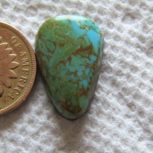 Pode incluir: Um cabochão de turquesa com uma cor azul-esverdeada e matriz marrom. O cabochão tem formato de lágrima e mede aproximadamente 2,5 cm de comprimento.