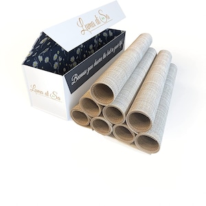 Op de afbeelding: Een set van acht beige placemats opgerold en verpakt in een witte doos met de tekst "Luma di Sa" en "Omdat je het beste in je leven verdient!" erop gedrukt.