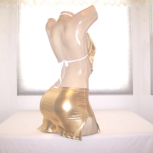May include: A gold metallic two-piece outfit on a mannequin. The top is a halter style with white ties, and the skirt is a mini skirt with a side slit. The outfit is displayed on a mannequin against a white background.