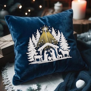 May include: A square, navy blue velvet pillow with an embroidered Christmas scene. The design features a star, a stable, and silhouettes of figures and animals in white thread. The background includes white pine trees and a golden glow.