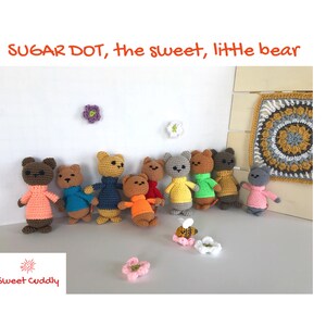 May include: A collection of handmade crochet bears in various colors, each wearing a sweater. The bears are brown, gray, and yellow, with sweaters in shades of pink, blue, orange, and green. The image includes the text "SUGAR DOT, the sweet, little bear" and "Sweet Cuddly".