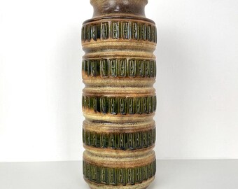 May include: A tall, cylindrical ceramic vase with a textured, layered design. The vase features bands of tan, brown, and green hues. The top and bottom are a darker brown, while the middle sections have a repeating rectangular pattern.