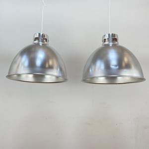 May include: Two silver pendant lights with a dome-shaped shade. The lights are hanging from white cords.