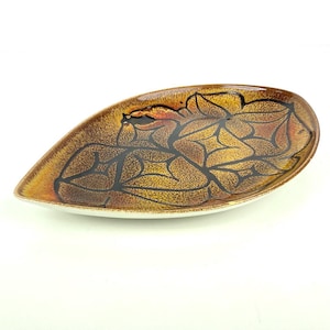 May include: A teardrop-shaped ceramic serving dish with a brown and gold speckled glaze. The dish features a black leaf-like pattern and a white rim. This decorative dish is ideal for serving snacks or displaying small items.