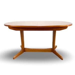 May include: An oval wooden dining table with a smooth, light brown finish. The table features a central seam indicating an extendable design, supported by two vertical legs connected by a horizontal base bar with four angled feet extending outwards.