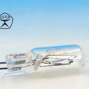 Puede incluir: Una bombilla de luz de vidrio transparente con dos clavijas metálicas. La bombilla tiene un pequeño filamento metálico en el interior y el texto "225 12 220V 1972" impreso en el lateral.