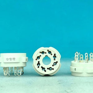 May include: Three white ceramic electrical components with metal pins. The component on the left has the text "0-10-72" printed on it. The component in the middle has a circular pattern of holes. The component on the right has the letter "E" printed on it.