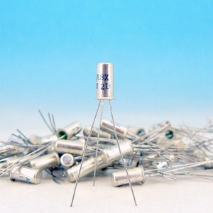 May include: A collection of silver-colored electronic components, with one standing upright. The upright component has three legs and text that reads "ASX 12D". The background is a gradient of white to light blue.