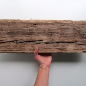 May include: A rustic wooden shelf with a natural brown finish and two metal hanging hooks. The shelf has a rough, weathered texture and is perfect for displaying decorative items.