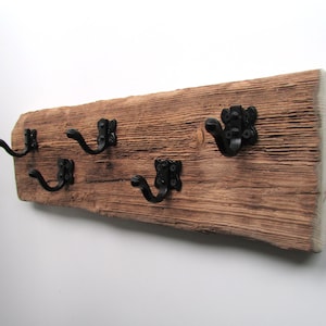May include: A rustic wooden wall hook with four black metal hooks. The wood has a natural, weathered finish.