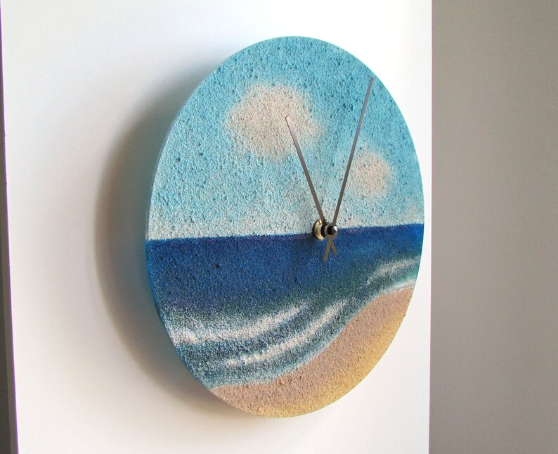 Pu&ograve; includere: Un orologio rotondo con un design a paesaggio marino blu e bianco. Il quadrante dell'orologio &egrave; realizzato in un materiale testurizzato che ricorda la sabbia. Le lancette dell'orologio sono argentate.