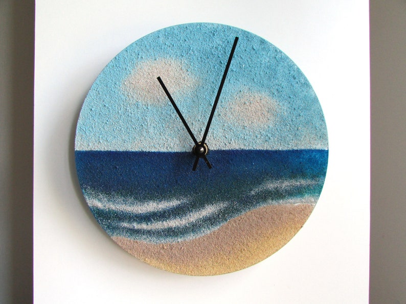 Pu&ograve; includere: Un orologio rotondo con un design a paesaggio marino blu e bianco. Il quadrante dell'orologio &egrave; dipinto per assomigliare a una scena di spiaggia con acqua blu, onde bianche e una spiaggia sabbiosa.