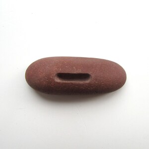 Peut inclure: Une pierre lisse de couleur brun rouge&acirc;tre avec une ouverture rectangulaire sculpt&eacute;e. La pierre est de forme ovale et a une texture rugueuse.