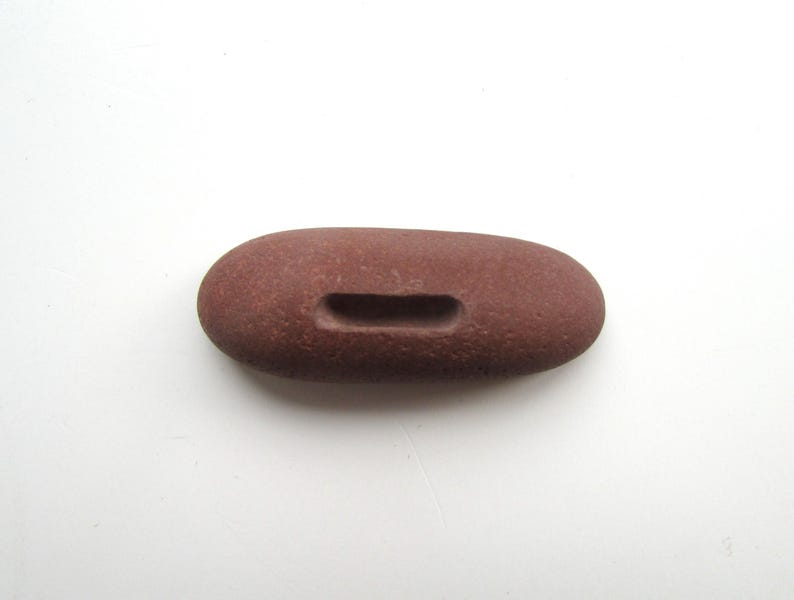 Peut inclure: Une pierre lisse de couleur brun rouge&acirc;tre avec une ouverture rectangulaire sculpt&eacute;e. La pierre est de forme ovale et a une texture rugueuse.