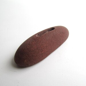 Peut inclure: Une pierre lisse de couleur brun rouge&acirc;tre avec une rainure creus&eacute;e. La pierre est de forme ovale et a une texture rugueuse.