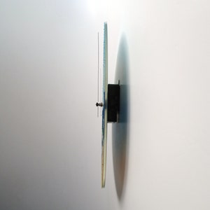 Pu&ograve; includere: Vista laterale di un orologio da parete rotondo con un design blu e bianco. L'orologio &egrave; montato su una parete bianca.