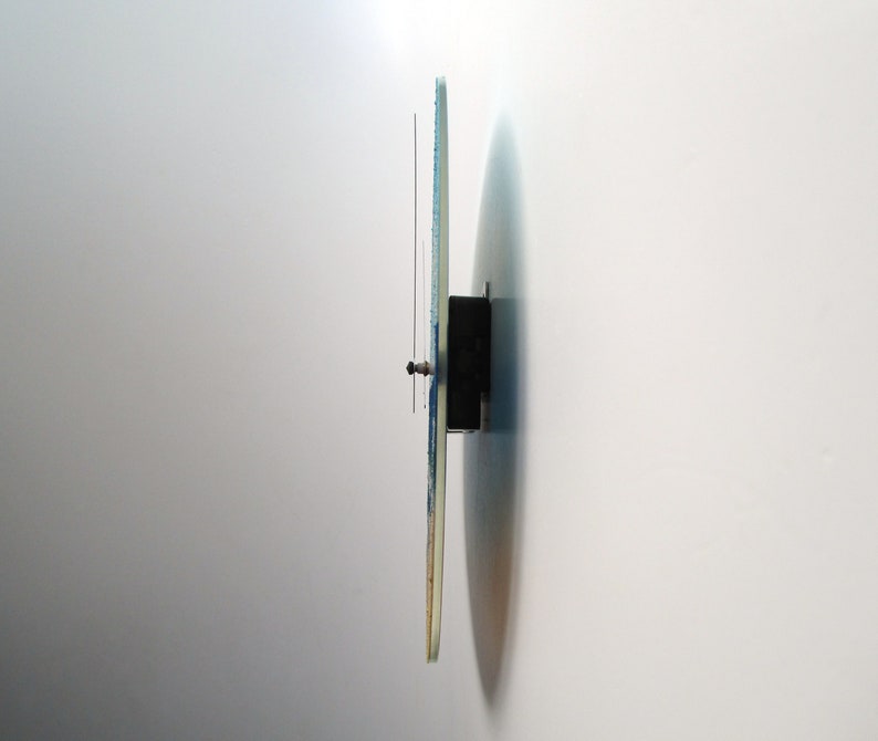 Pu&ograve; includere: Vista laterale di un orologio da parete rotondo con un design blu e bianco. L'orologio &egrave; montato su una parete bianca.