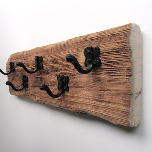 May include: A rustic wooden coat rack with four black metal hooks. The wood has a natural, weathered finish.