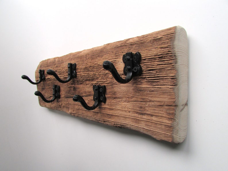 May include: A rustic wooden coat rack with four black metal hooks. The wood has a natural, weathered finish.