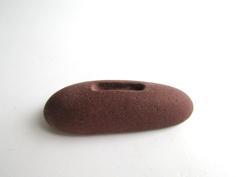 Peut inclure: Une pierre lisse de couleur brun rouge&acirc;tre avec une rainure creus&eacute;e au centre. La pierre est de forme ovale et a une texture rugueuse.