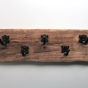 May include: A rustic wooden wall mounted coat rack with four black metal hooks. The wood is weathered and has a natural finish.