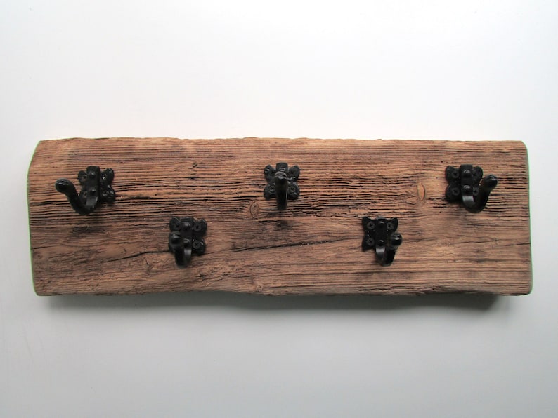 May include: A rustic wooden wall mounted coat rack with four black metal hooks. The wood is weathered and has a natural finish.