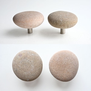May include: Four natural stone knobs with a smooth, rounded surface and a silver metal stem. The knobs are a light brown color with a speckled texture.