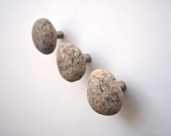 May include: Three cabinet knobs featuring rounded, natural stone heads with a speckled brown and grey texture. Each stone is securely attached to a short, cylindrical metal base that extends outward from the mounting surface.