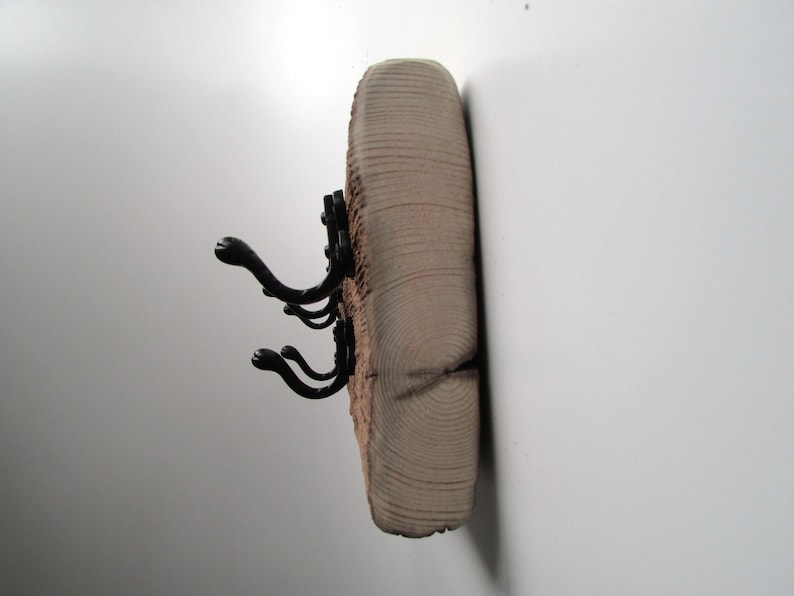 May include: A wooden wall-mounted coat rack with three black metal hooks. The wood has a natural, rustic finish and shows the grain of the wood.