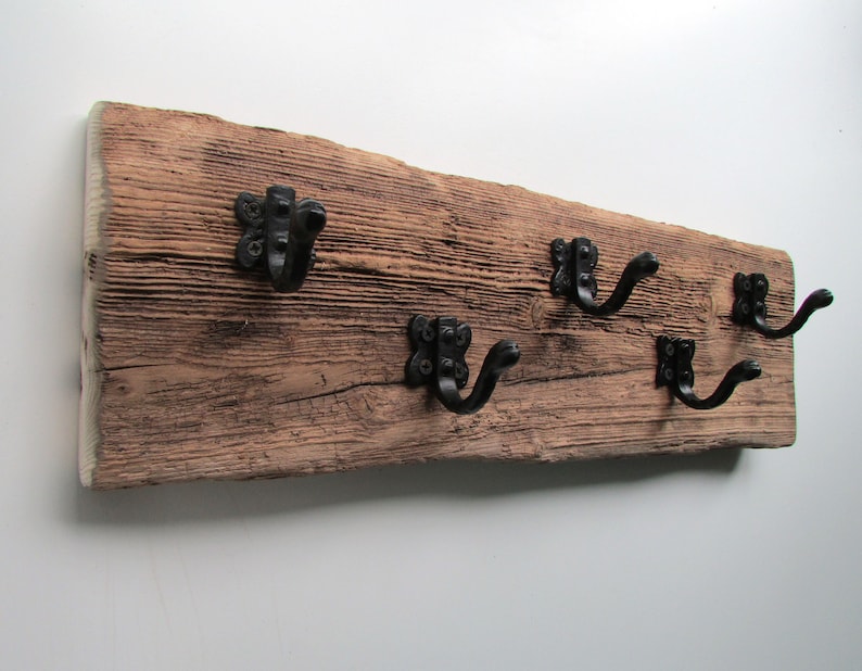 May include: A rustic wooden wall-mounted coat rack with four black metal hooks. The wood has a natural, weathered finish.