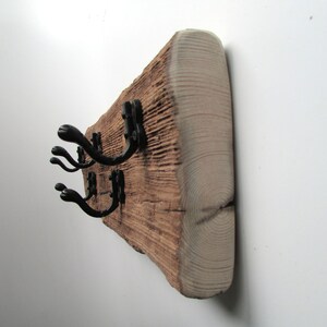 May include: A rustic wooden coat rack with black metal hooks. The wood has a natural, weathered finish and is mounted on a white wall.