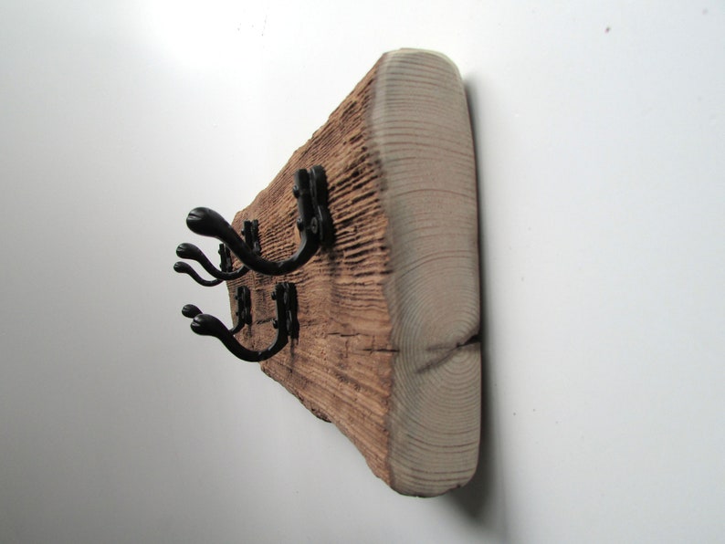May include: A rustic wooden coat rack with black metal hooks. The wood has a natural, weathered finish and is mounted on a white wall.