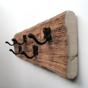 May include: A rustic wooden wall hook with three black metal hooks. The wood has a natural, weathered finish and is a reclaimed piece of lumber.