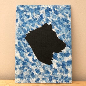 May include: A black silhouette of a dog's head is painted on a white canvas with a blue and white splatter paint background.