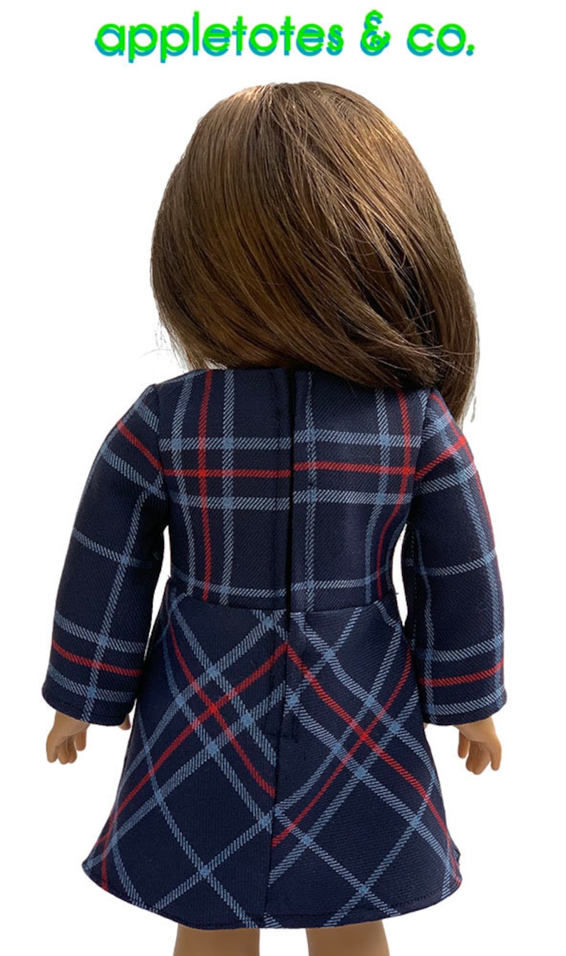 May include: A blue and red plaid dress with long sleeves for a doll. The dress has a zipper in the back.