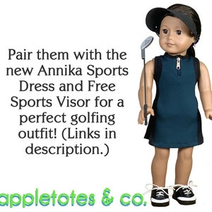 May include: A doll wearing a teal sleeveless dress with a black stripe down the side, a black visor, and black and white sneakers. The doll is holding a golf club. The text "Pair them with the new Annika Sports Dress and Free Sports Visor for a perfect golfing outfit! (Links in description.) appletotes & co." is at the bottom of the image.