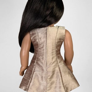 May include: A sleeveless dress for a doll, made of a shimmery gold fabric. The dress has a fitted bodice and a flared skirt.